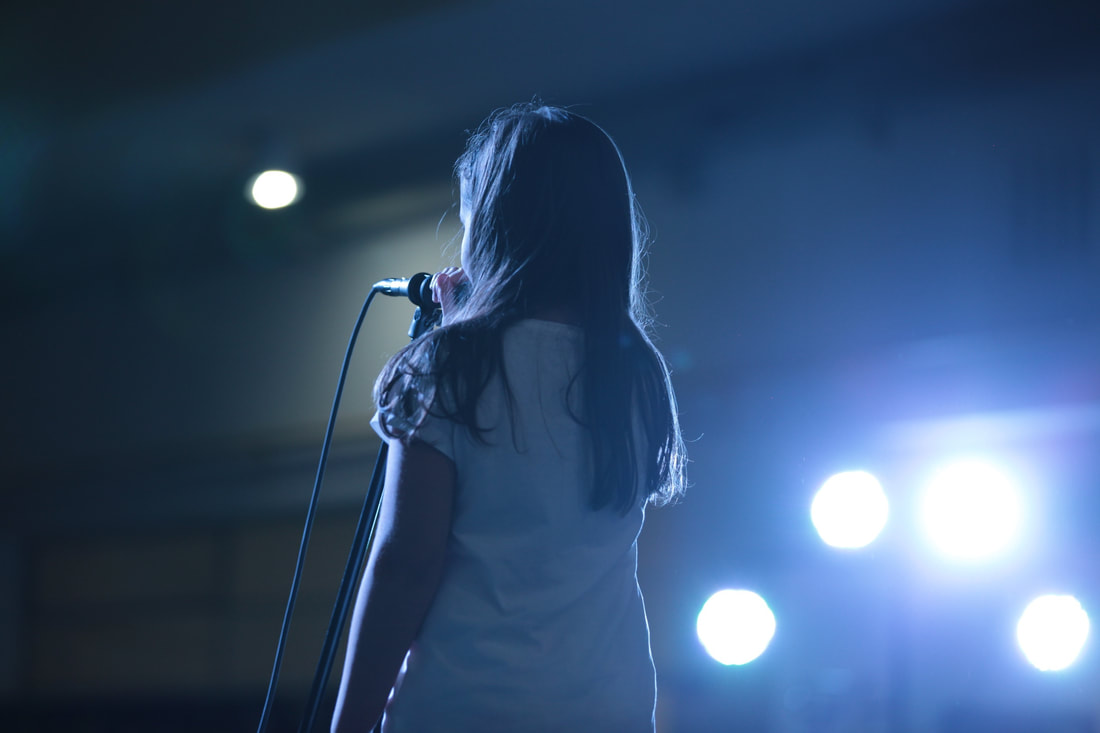 Picture of little girl at mic on stage from the back